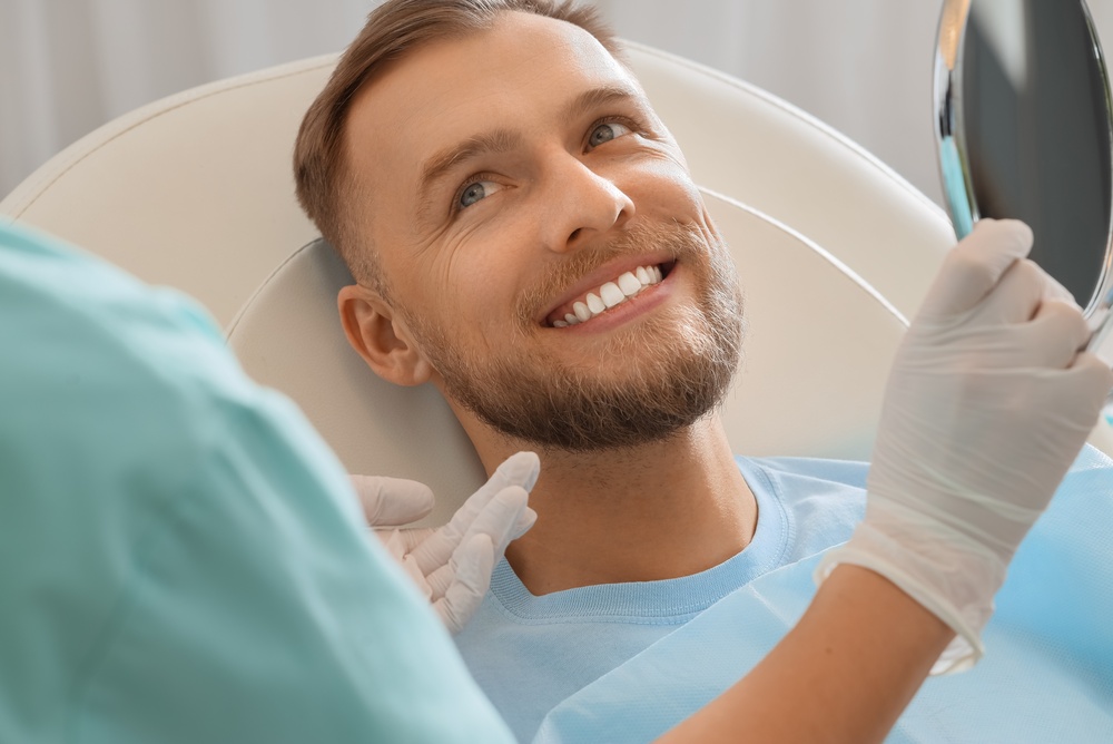 Young man with dentist looking in mirror at hospital, closeup