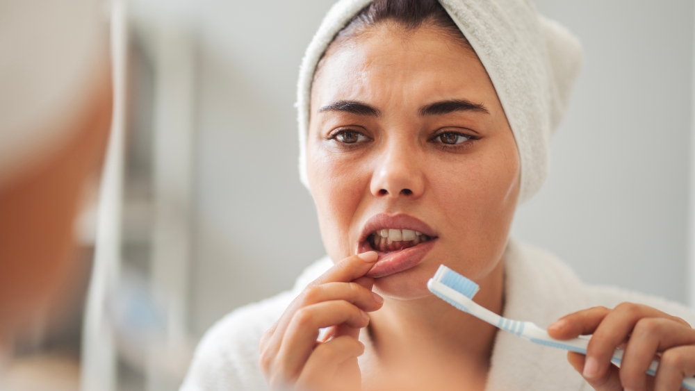 Gum sensitivity, a common sign of gingivitis Woman wincing in discomfort while brushing her teeth and touching her gum