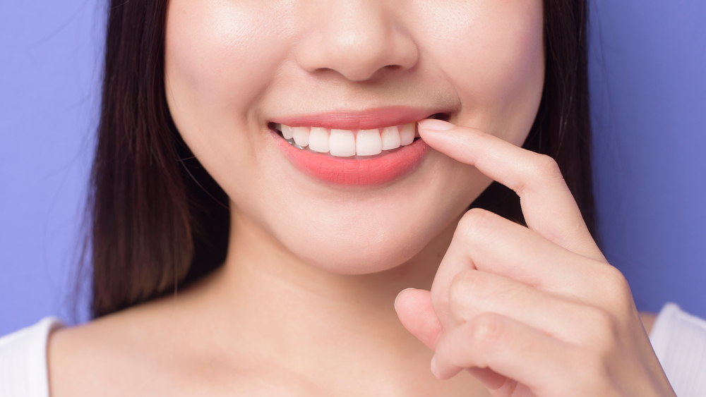a young smiling beautiful woman is showing and pointing her healthy straight white teeth over purple background studio