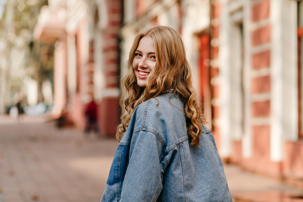 Young woman smiling brightly outdoors, representing the healthy, aligned smiles achieved through orthodontics in the Norfolk community 