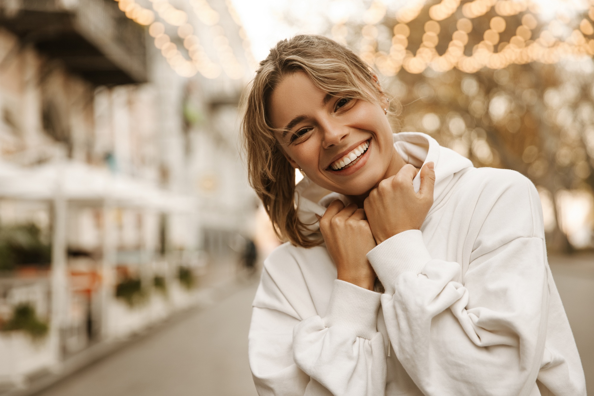 Woman in a white hoodie smiling outdoors with a bright, healthy smile 