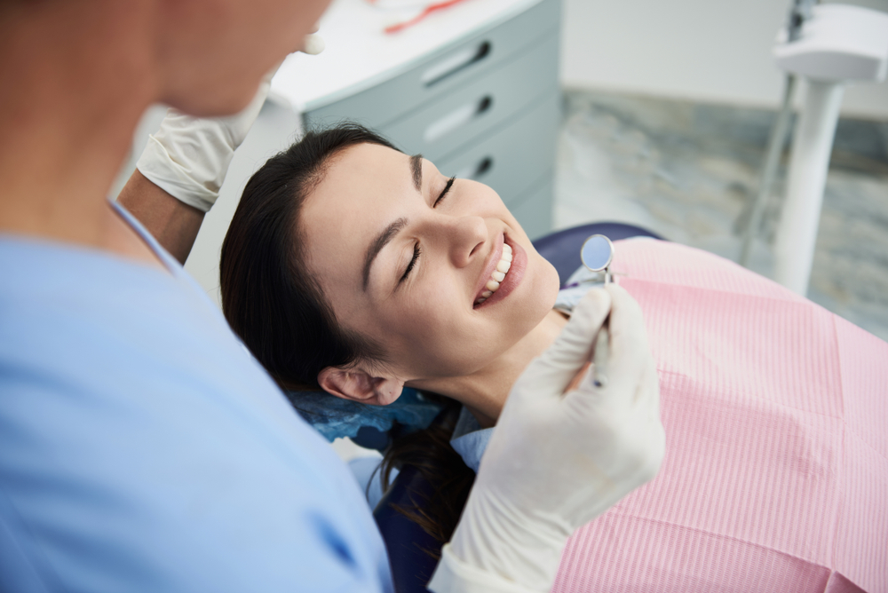 Woman smiling peacefully with her eyes closed while a dentist holds a mirror near her mouth