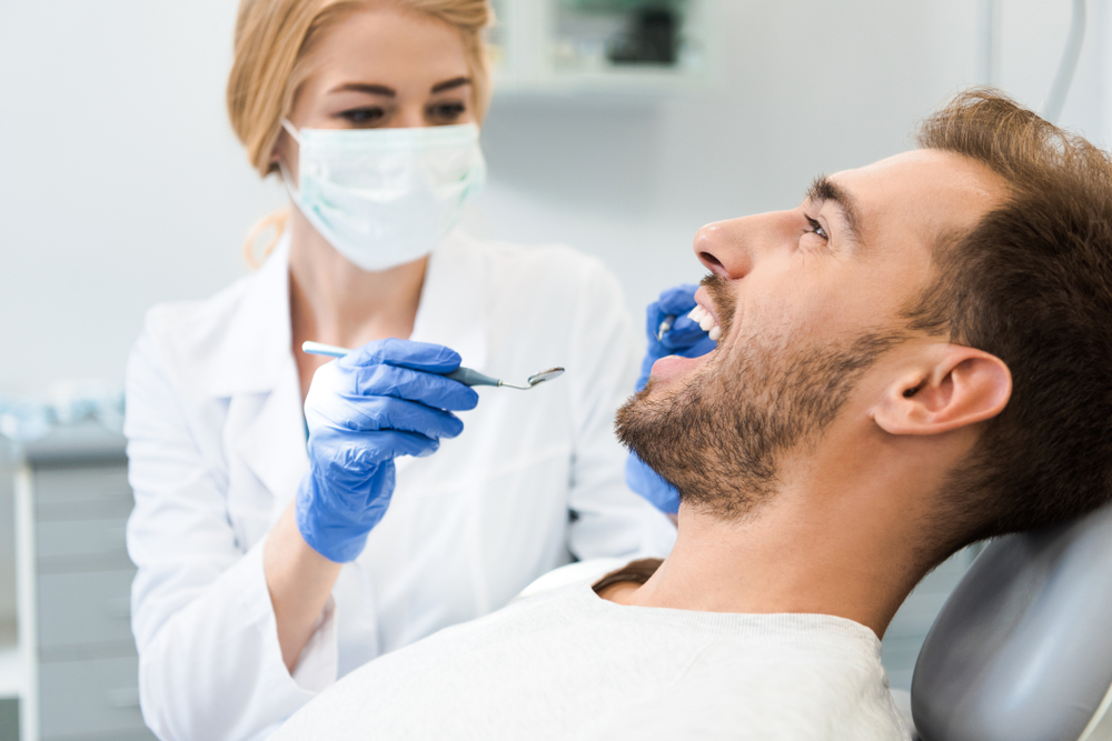 Dentist examining a patient's teeth with a mirror and explorer during a restorative dentistry visit in Hampton Roads 