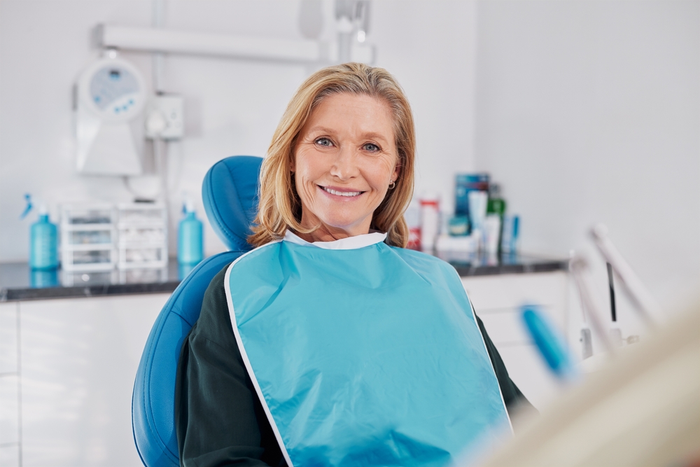 Comfortable denture fittings in Norfolk Mature woman smiling while seated in a dental chair