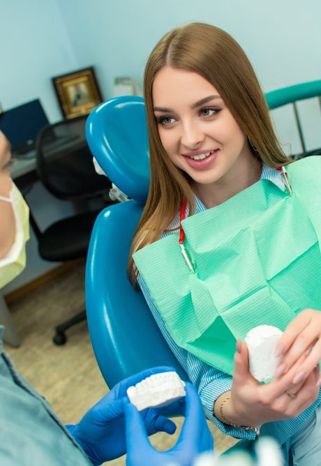 Young woman in a dental chair holding a dental mold while speaking with her dentist
