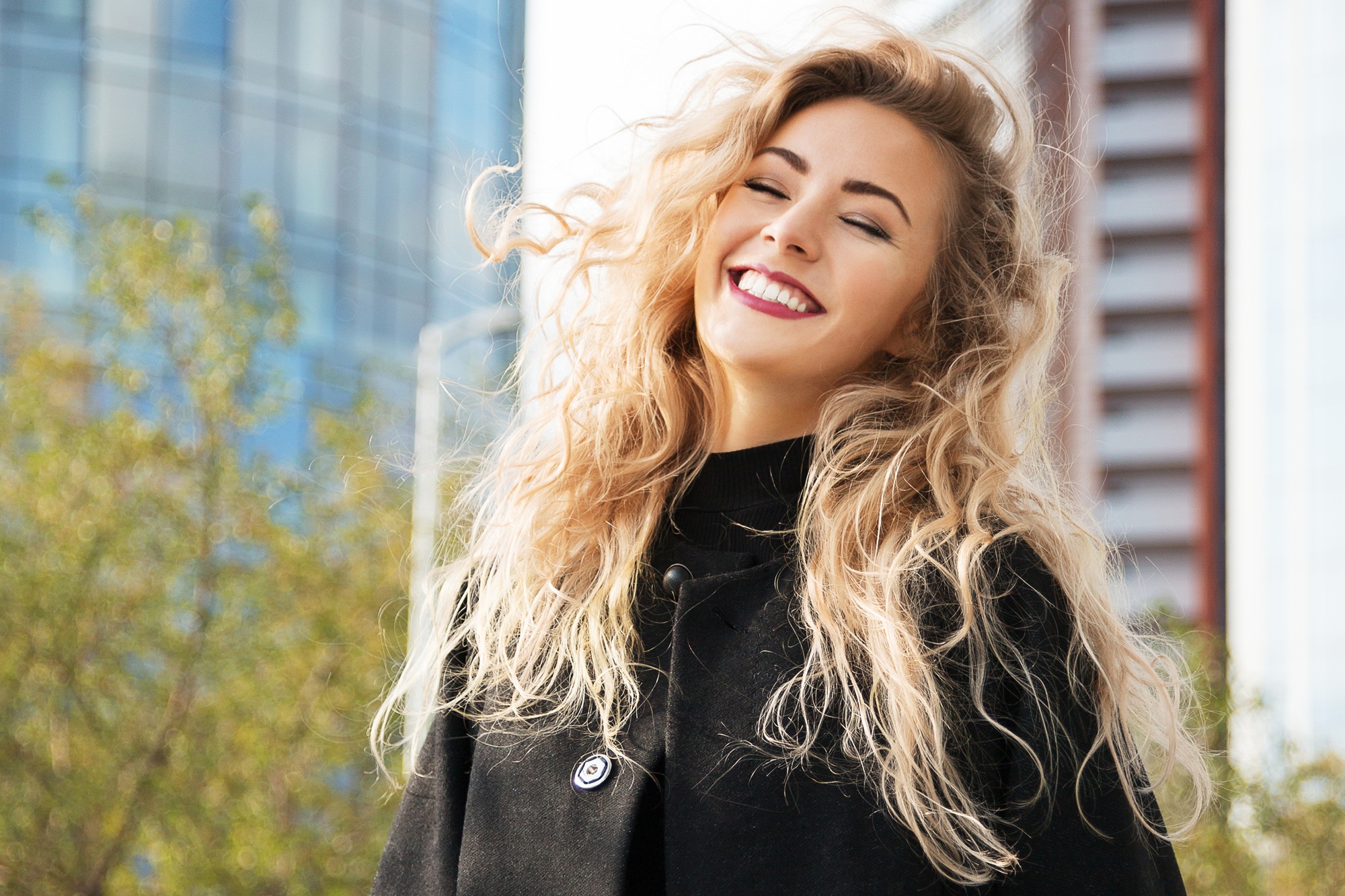 Woman laughing joyfully outdoors with her eyes closed