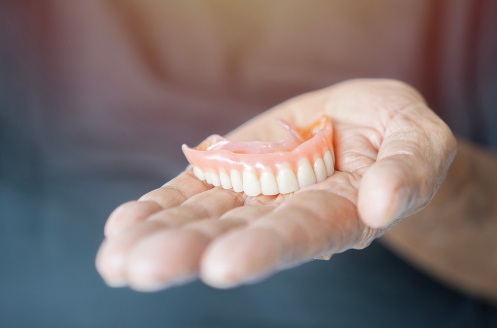 Custom dentures and partials in Virginia Beach, VA, The Foleck Center Full denture held in the palm of a hand, representing custom dentures and partials at The Foleck Center, Virginia Beach, VA