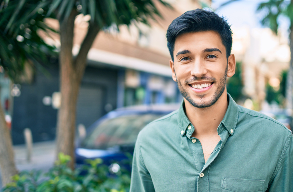 Young man smiling outdoors with straight teeth after traditional braces treatment in Norfolk 