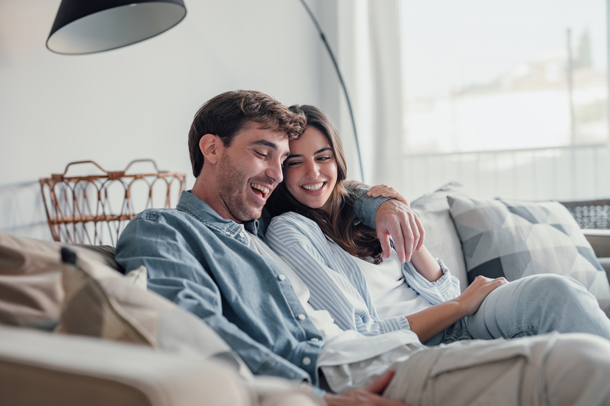 Man and woman laughing together while sitting on a couch at home