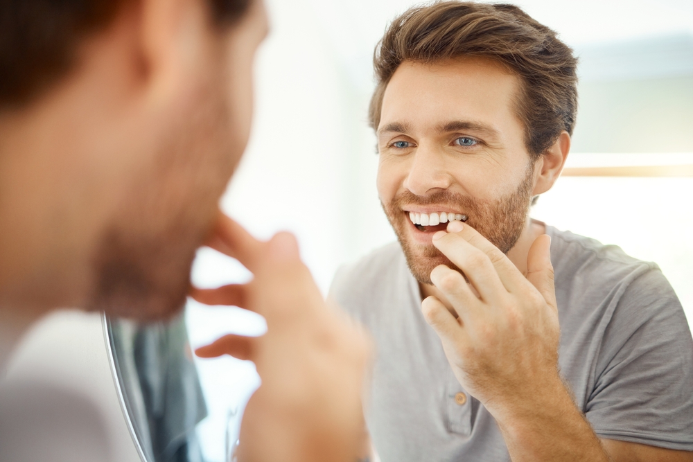 Smile Check After Implants: Virginia Beach Patient Man checking his smile in the mirror after dental implant treatment in Virginia Beach