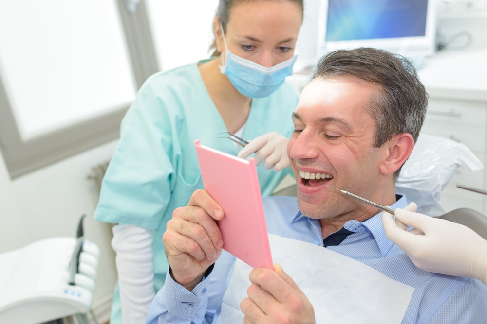 Reviewing gum health results in Hampton Roads Patient smiling while looking at his teeth in a hand mirror during a dental visit