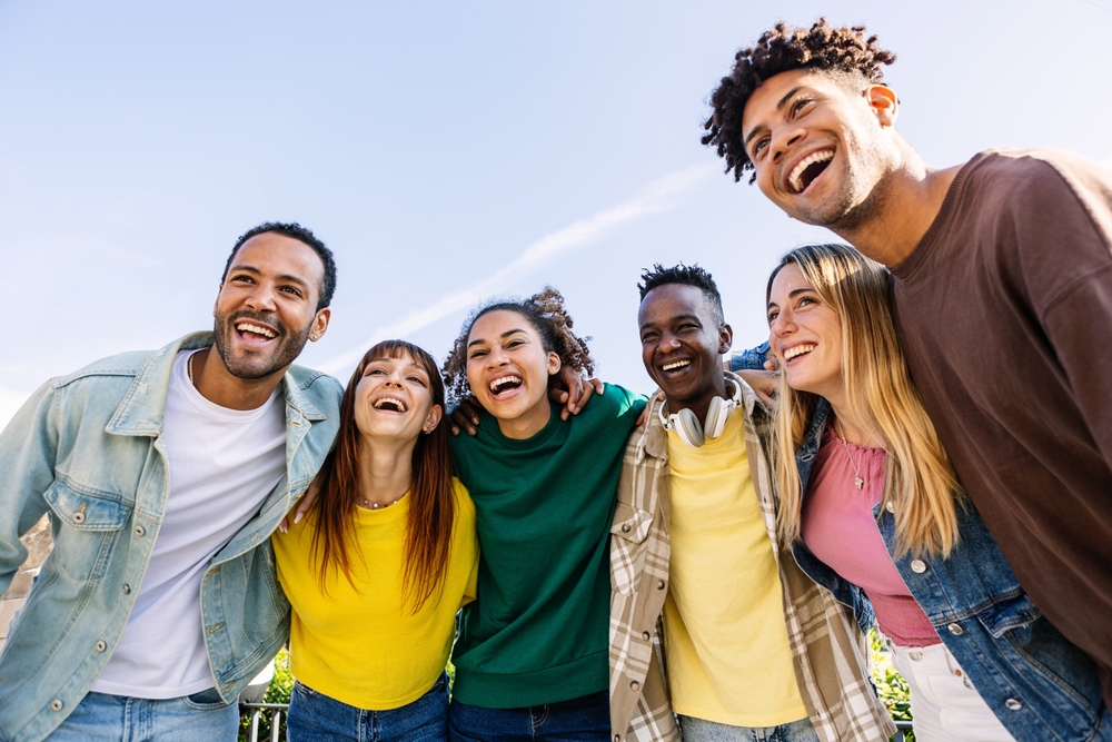 Diverse group of young adults laughing outdoors with bright, confident smiles, representing teeth whitening results at The Foleck Center, Virginia Beach, VA 