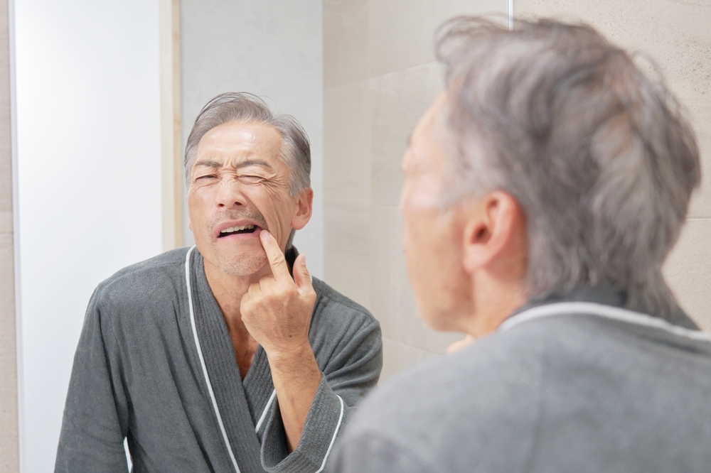 Older man wincing while pointing to his gum in a bathroom mirror