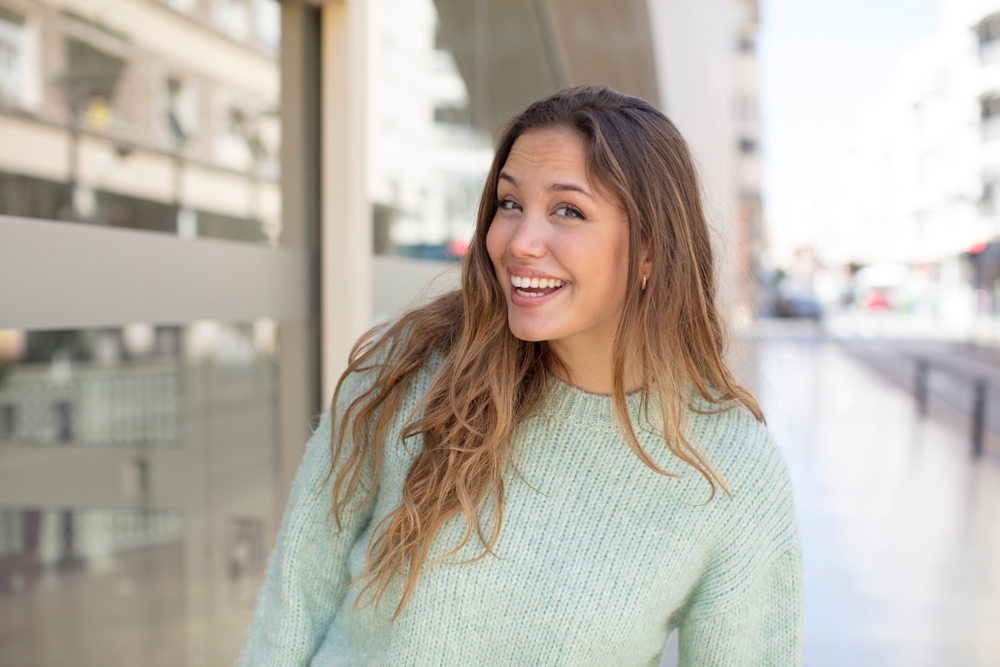 Healthy smile, gum disease care in Hampton Roads Woman in a green sweater smiling and looking back over her shoulder outdoors