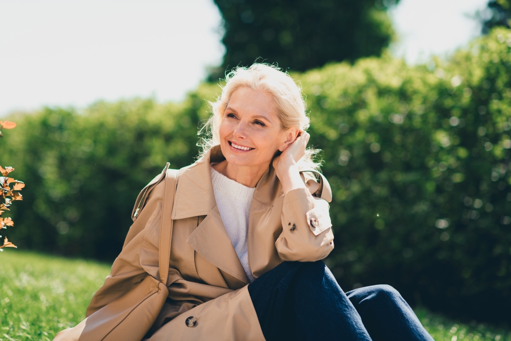 Confident smile, dentures and partials in Norfolk Mature woman with blonde hair smiling outdoors in a trench coat