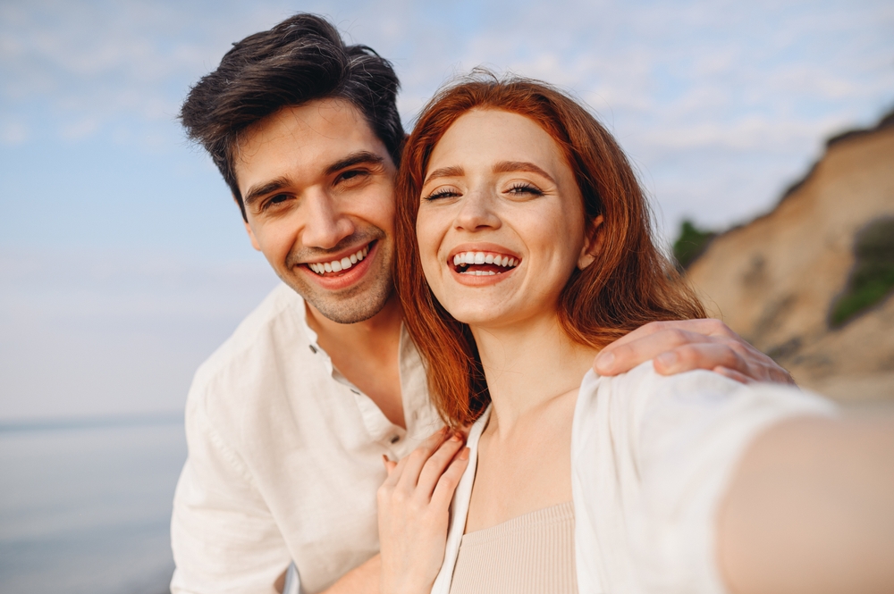 Confident smiles after emergency dental care, The Foleck Center, Hampton Roads, VA Smiling couple taking a selfie at the beach with bright, healthy teeth, reflecting confidence after emergency dental care at The Foleck Center, Hampton Roads, VA