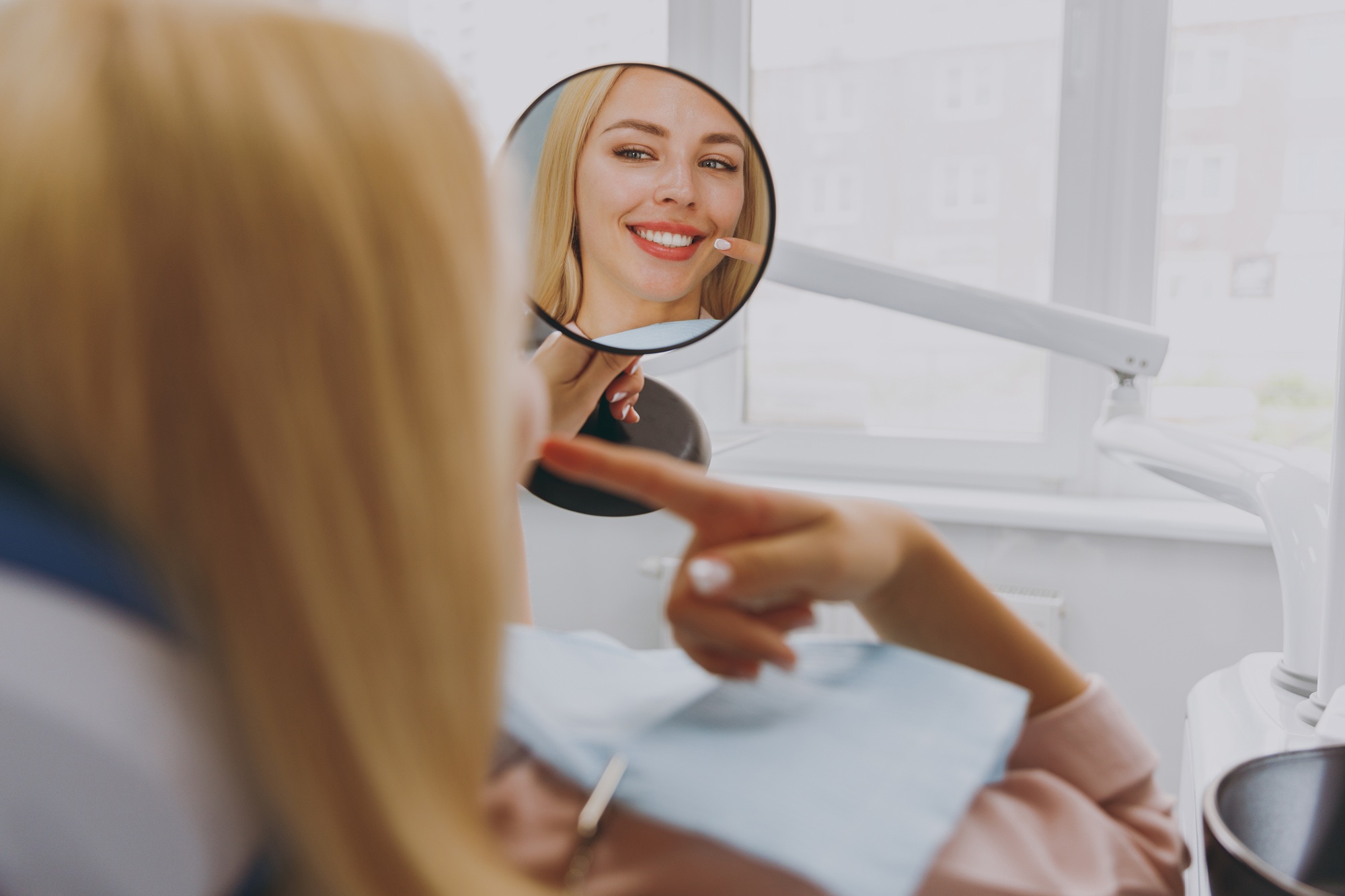 Patient admiring her smile in a hand mirror during a dental visit 