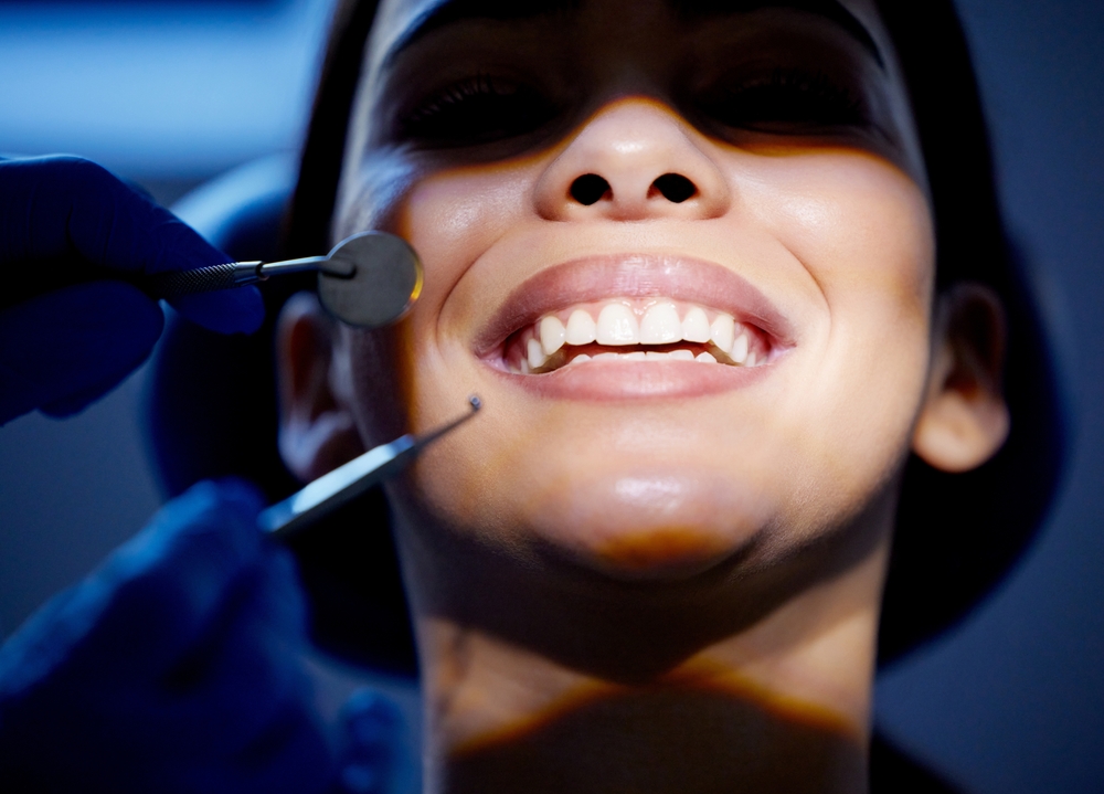Dentist holding a mirror and explorer to examine a patient's teeth up close 