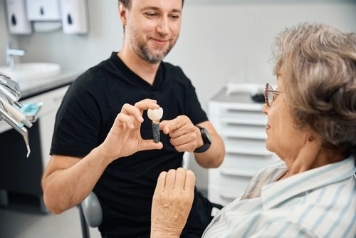 Explaining dental implants in Hampton Roads Dentist showing a dental implant model to an elderly patient in the office