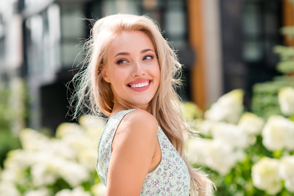 Woman smiling outdoors among blooming flowers after a stress-free sedation visit in the Norfolk community 
