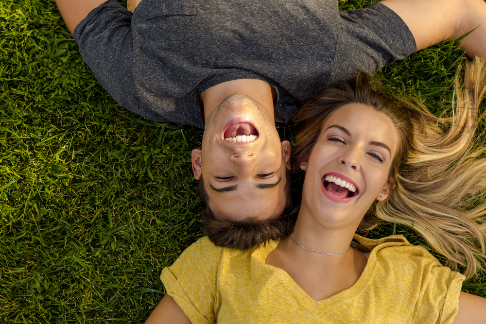 Couple laughing together on the grass, showing off their smiles after cosmetic dentistry in Virginia Beach 