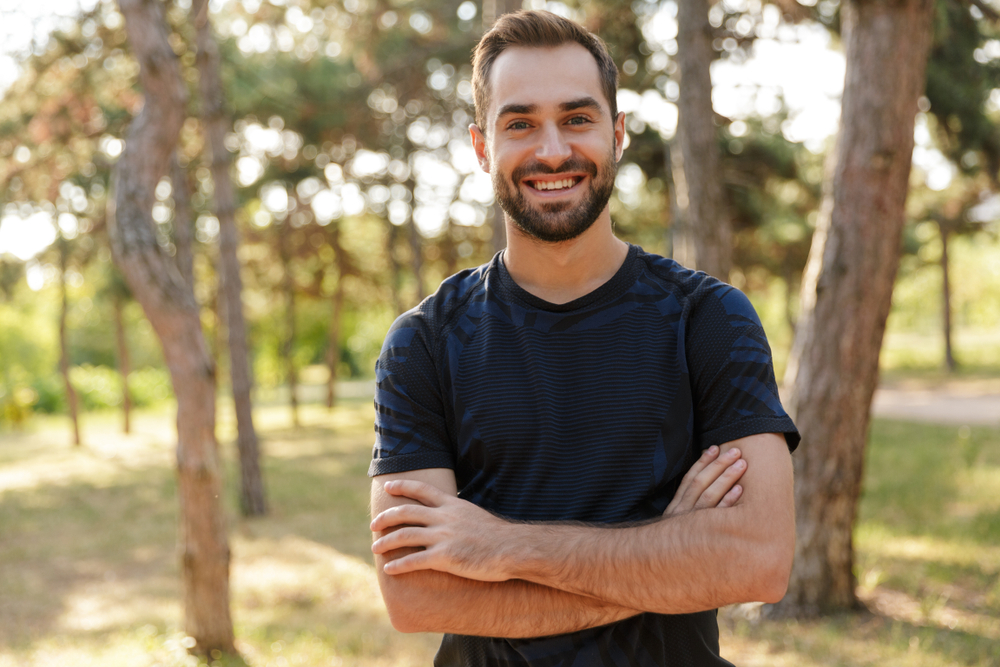 Happy male patient showing off smile results from cosmetic dentistry at The Foleck Center, Virginia Beach Confident man with a bright smile standing outdoors after cosmetic dentistry treatment at The Foleck Center in Virginia Beach